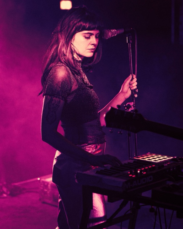 Lotti, Sängerin der Leipziger Band glu:, live am Mikrofon und Keyboard in pinkem Bühnenlicht