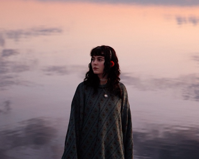 Lotti, Sängerin der Leipziger Band glu:, in der Abenddämmerung an einem See, mit Retro-Kopfhörern