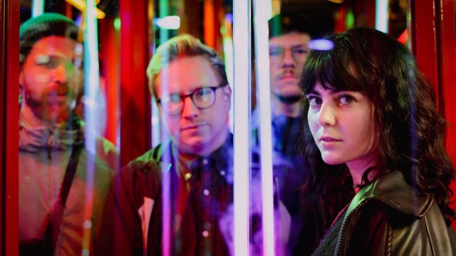 Vorschaubild zum Musikvideo delight von glu: – die vier Bandmitglieder zwischen bunten Neonröhren